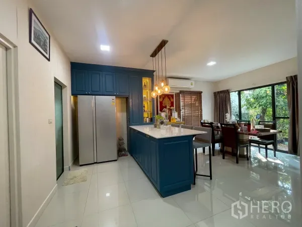 Detached House for sale in Bang Phli, Samut Prakan - Open-plan kitchen and dining with blue cabinetry, large island, pendant lights and garden views.