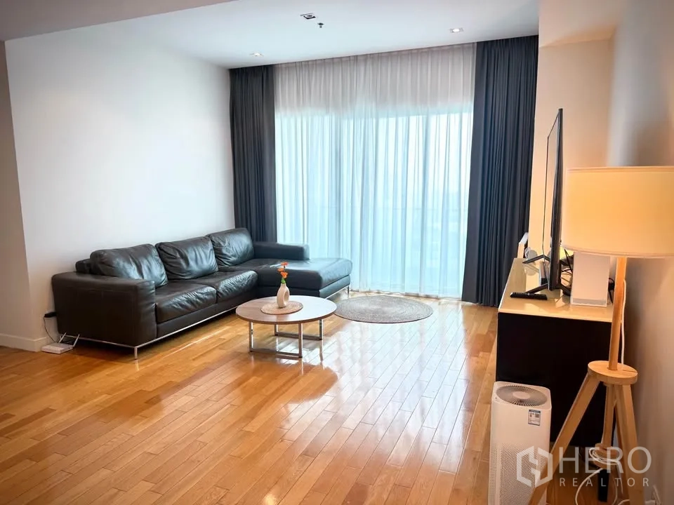 คอนโด for rent or sale in Khlong Toei, Bangkok - ห้องนั่งเล่นโซฟาหนังสีดำ ตู้วางทีวี และหน้าต่างสูงเต็มบาน.