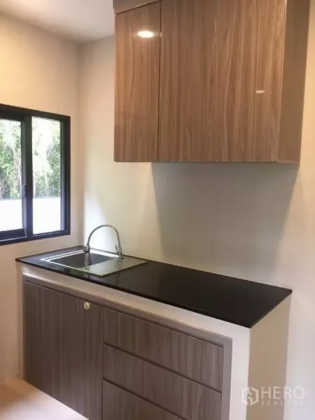 Detached House for rent in Samut Prakan - Compact pantry with glossy wood cabinets, black countertop and a sink under the window.