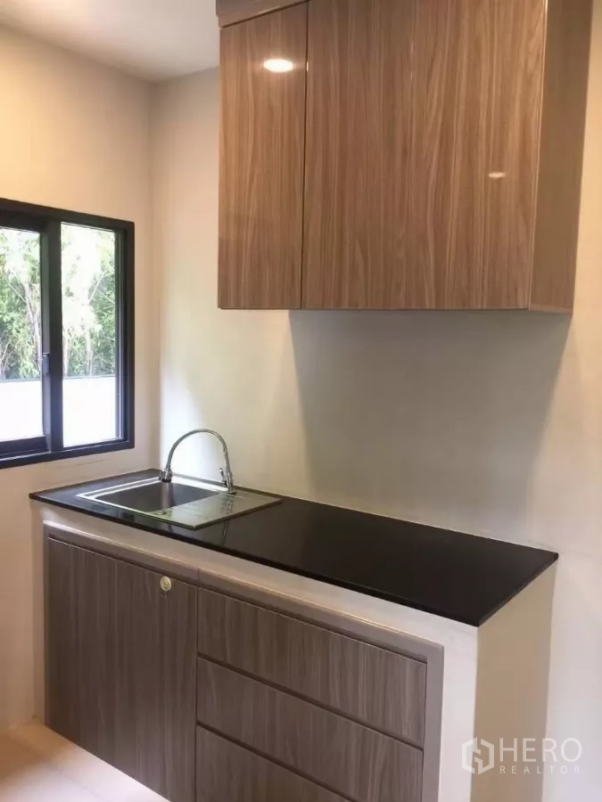 Detached House for rent in Samut Prakan - Compact pantry with glossy wood cabinets, black countertop and a sink under the window.