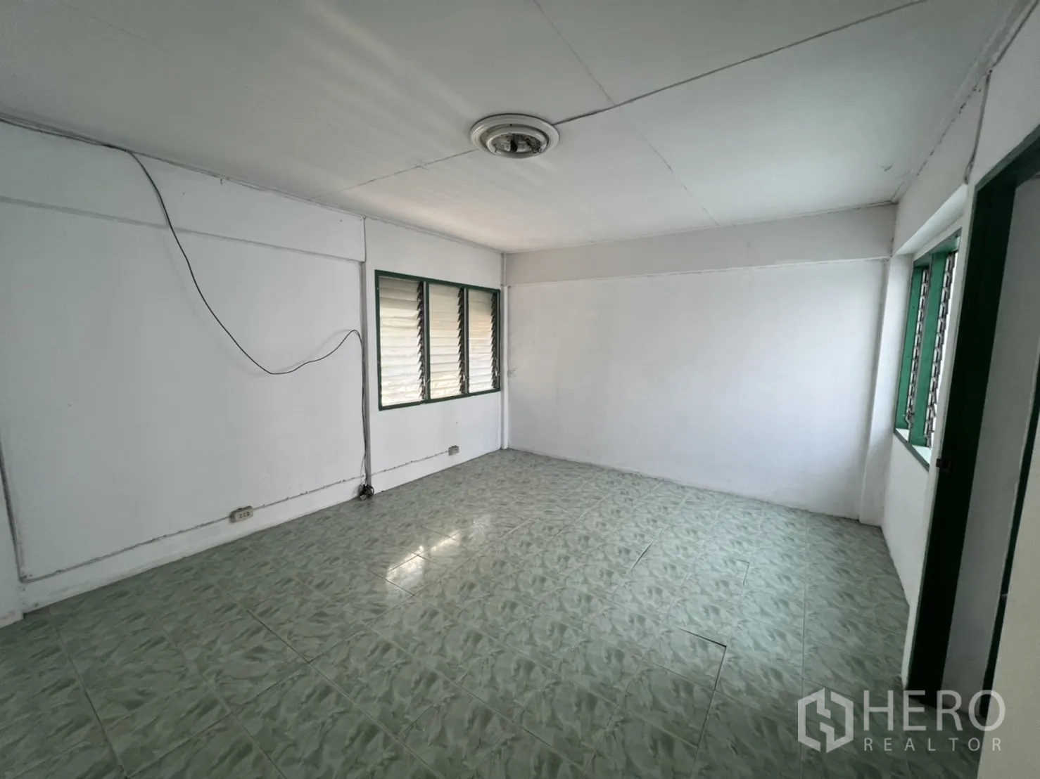Townhouse for sale in Watthana, Bangkok - Large upper room with ceiling light and windows, a blank canvas to redesign.
