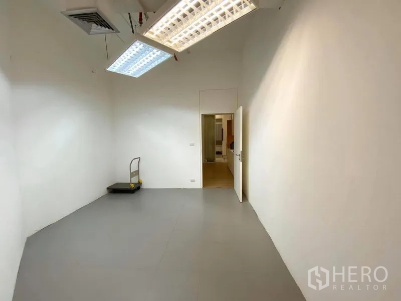 Office Space for rent in Bangkok - Utility or storage room with high ceiling, white walls and bright fluorescent lighting.