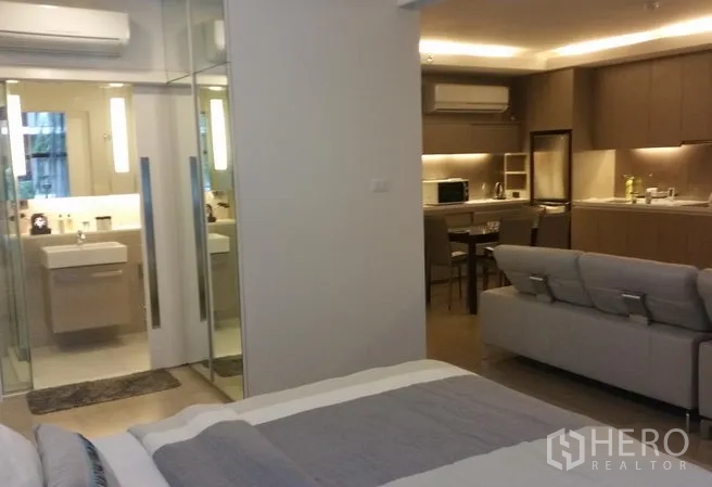Condominium for rent or sale in Watthana, Bangkok - View from bedroom to open‑plan living with kitchenette, dining area, sofa and bathroom with glass door.