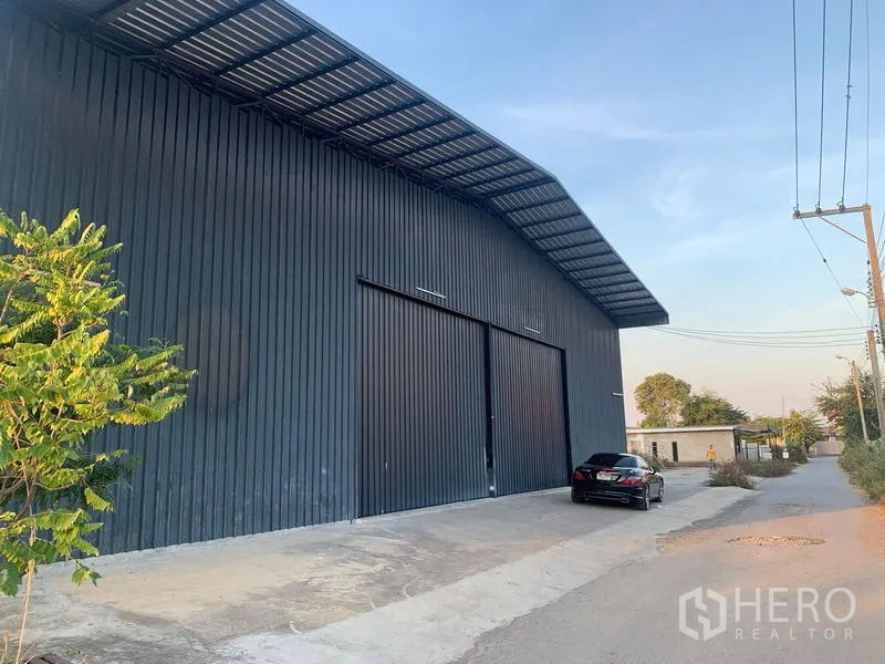 货栈 出租在Khan Na Yao, Bangkok - 仓库外观，深色金属立面，超大推拉门、雨棚与门前车道。