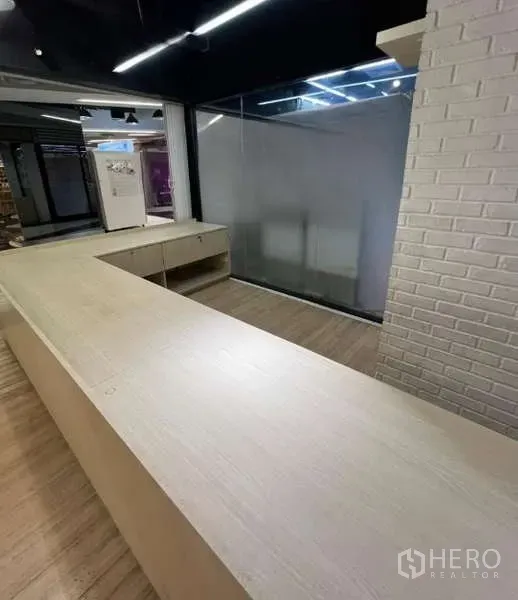 零售空间 出租在Watthana, Bangkok - 零售店内景，L形木质服务台，玻璃隔断与白色砖墙，配轨道灯。