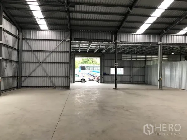 Warehouse for rent in Pak Kret, Nonthaburi - Open storage floor facing a large roller door with vehicles visible outside.