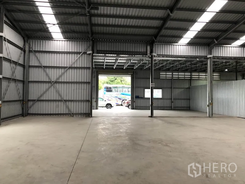 Warehouse for rent in Pak Kret, Nonthaburi - Open storage floor facing a large roller door with vehicles visible outside.