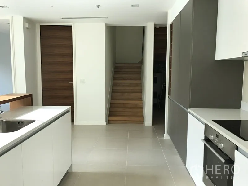 公寓 出租在Khlong San, Bangkok - 开放式厨房连接木楼梯，白色台面与高柜一体