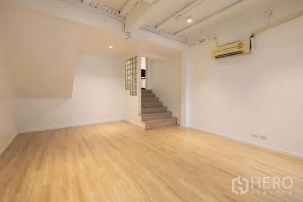 联排别墅 出租在Khlong Toei, Bangkok - 开放式起居区，木地板与射灯，台阶通往抬高空间。