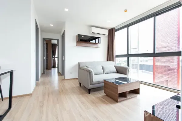 Condominium for rent in Watthana, Bangkok - Bright living room with floor-to-ceiling windows, gray sofa and light wood floors at Taka Haus Ekkamai.