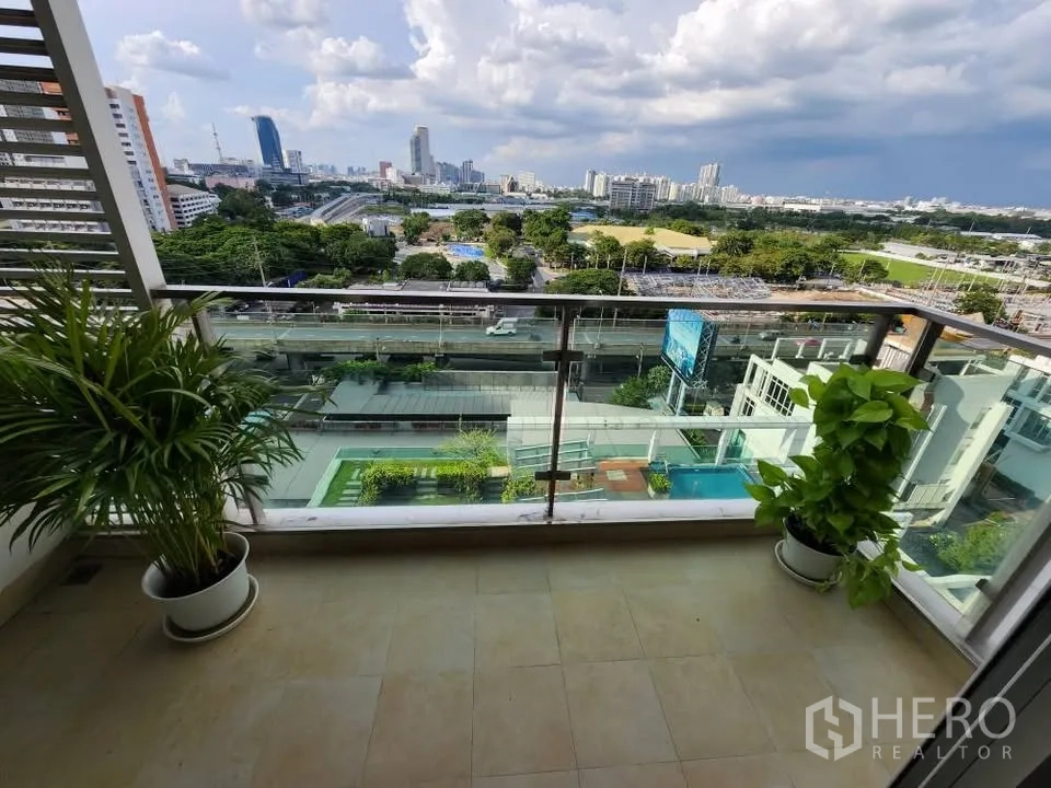 Condominium for rent in Huai Khwang, Bangkok - Spacious balcony with glass railing and plants overlooking pool and Bangkok skyline.
