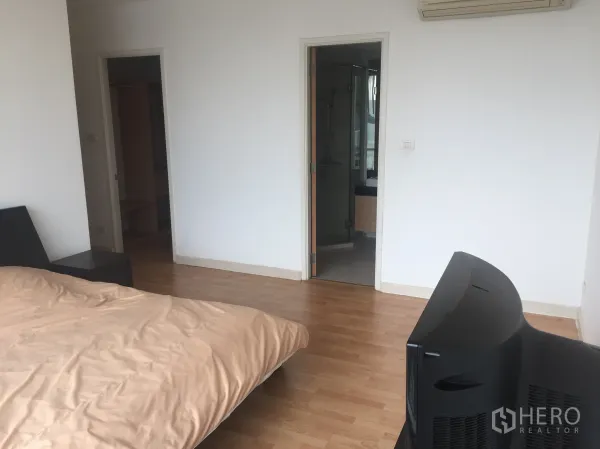 Condominium for rent or sale in Watthana, Bangkok - Spacious bedroom with wood flooring, TV console and access to an ensuite bathroom.