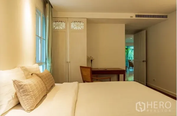 Apartment for rent in Bang Rak, Bangkok - Bedroom angle showing bed, decorative-panel wardrobe, desk and view toward the living area.