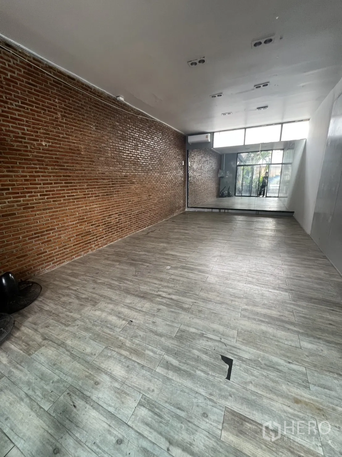 พื้นที่ขายปลีก ให้เช่า - ภายในพื้นที่ค้าปลีกแบบเปิด ผนังอิฐเปลือย พื้นลายไม้ และกระจกเงาด้านหลัง
