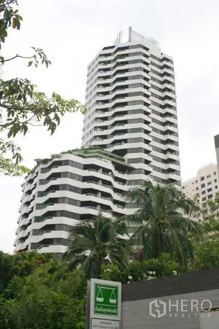 Condominium for rent in Watthana, Bangkok - High-rise condominium tower with stacked balconies framed by tropical trees.