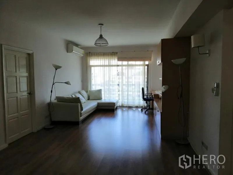 Condominium for rent in Watthana, Bangkok - Spacious living room with wood floors, large windows, and work desk.