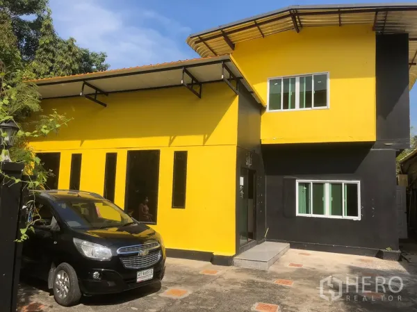 บ้าน ให้เช่าในKhlong Toei, Bangkok - บ้านเดี่ยวสองชั้นโทนเหลืองดำ หน้าต่างบานเลื่อน พร้อมลานจอดรถภายในรั้ว ใต้ท้องฟ้าโปร่ง