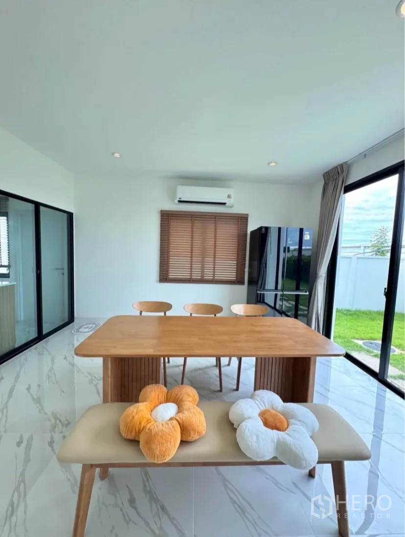 Detached House for rent in Samut Prakan - Dining area with wooden table and bench beside full-height glass doors to the garden.