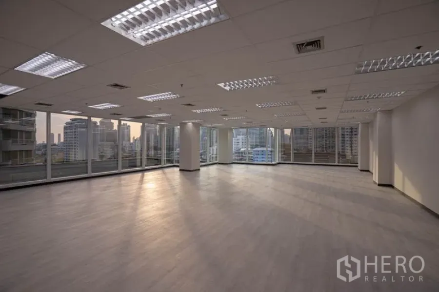 Office Space for rent in Bang Rak, Bangkok - Open-plan office at dusk with panoramic glazing and warm natural light across wood-look floors.