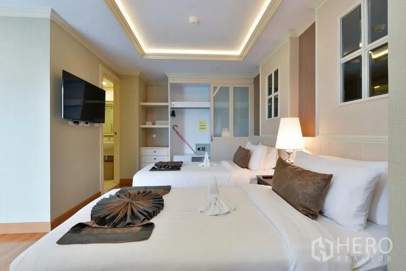 Apartment for rent in Khlong Toei, Bangkok - Cozy bedroom with two beds, built-in wardrobe and wall-mounted TV.