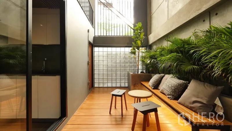 Townhouse for rent in Khlong Toei, Bangkok - Indoor–outdoor courtyard with timber deck, built-in bench, cushions and lush plants by the pantry.