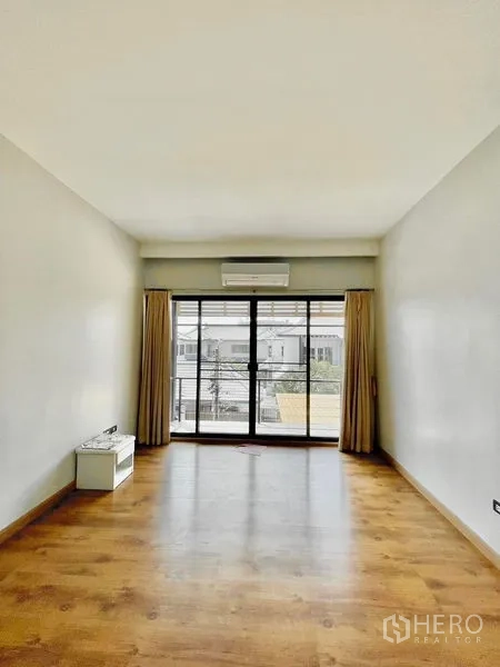 Townhouse for rent in Khlong Toei, Bangkok - Spacious room with wood flooring and wide balcony doors letting in natural light.