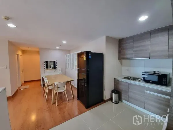 Condominium for rent in Huai Khwang, Bangkok - Open kitchen with wood cabinets, black refrigerator and adjacent dining area.