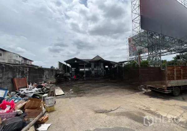 Land for sale in Bang Kapi, Bangkok - Front yard view with materials and a truck beside a warehouse-style shed and billboard frame on an industrial land plot.