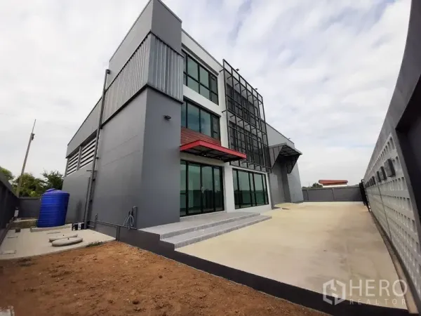 โรงงาน ให้เช่าหรือขายในLam Luk Ka, Pathum Thani - ภาพด้านข้างแสดงลานคอนกรีตกว้าง ประตูรั้ว และจุดโหลดสินค้า