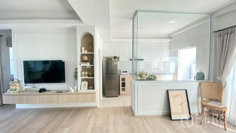 Townhouse for rent in Prawet, Bangkok - Built-in TV wall beside a glass-enclosed white kitchen with subway tiles and a stainless-steel fridge in an airy townhouse.