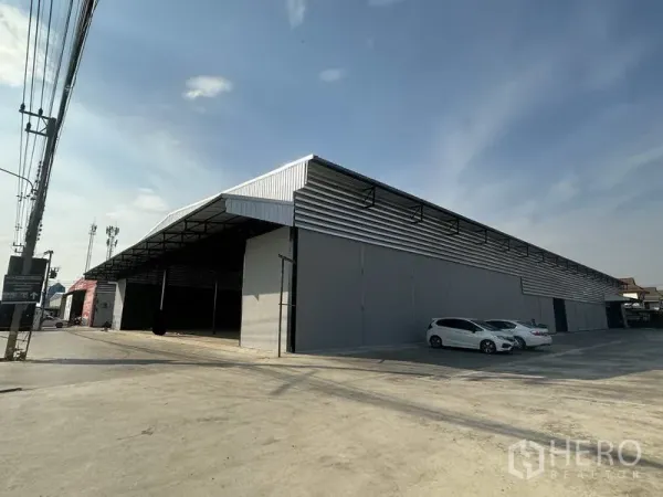 คลังสินค้า ให้เช่าในLam Luk Ka, Pathum Thani - ภาพเฉียงอาคารโกดังสีเทายาว มีหลังคาคลุมลานขนส่งและที่จอดรถบนลานปูน