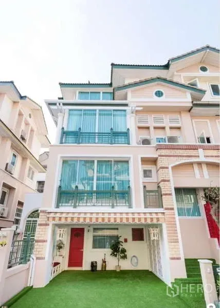 Townhouse for rent in Lat Phrao, Bangkok - Townhouse exterior with striped awning, red front door and wrought-iron balcony rails.