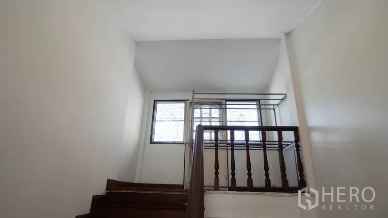 Townhouse for rent in Khlong Toei, Bangkok - Stair landing with wood banister and window bringing in natural light.