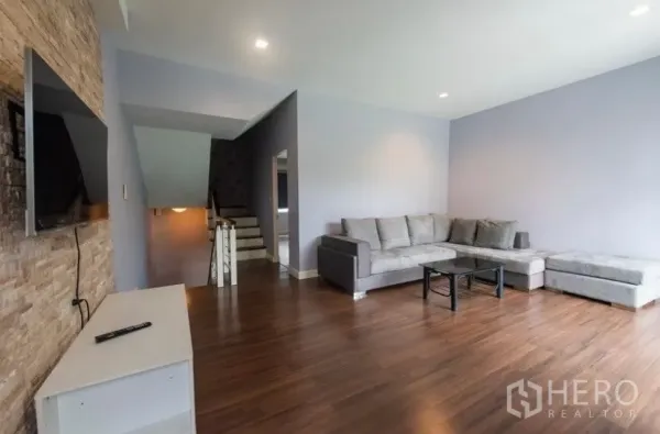 ทาวน์เฮาส์ ให้เช่าในSuan Luang, Bangkok - ห้องนั่งเล่นชั้นบน พื้นไม้ โซฟาเข้ามุมสีเทา และทีวีติดผนังลายหิน