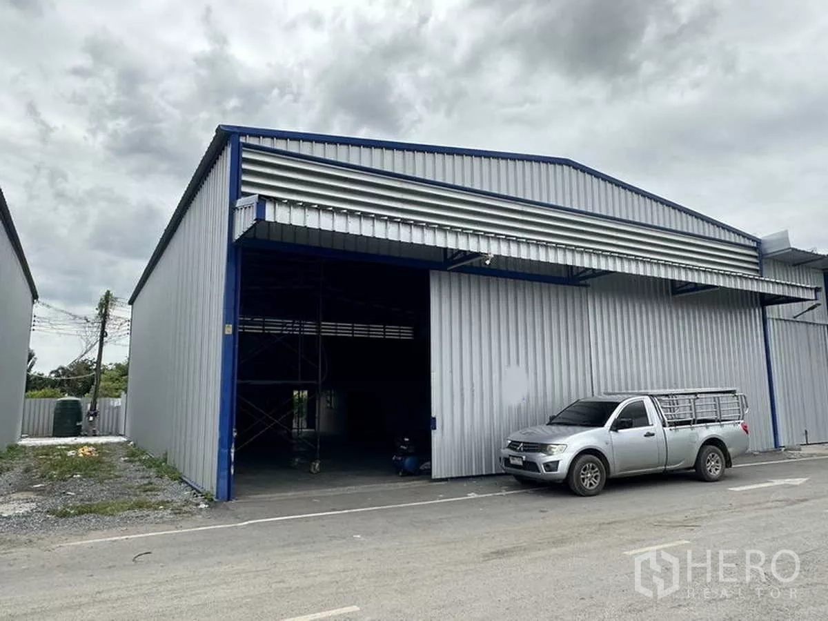 货栈 出租在Khlong Luang, Pathum Thani - 山墙顶仓库外立面，大型卷门开启，皮卡停靠在装卸区。