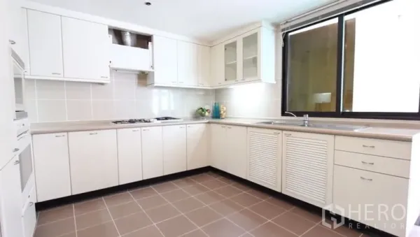 房间 出租在Khlong Toei, Bangkok - 明亮U形厨房，白色橱柜、炉灶、充足台面和大窗户。