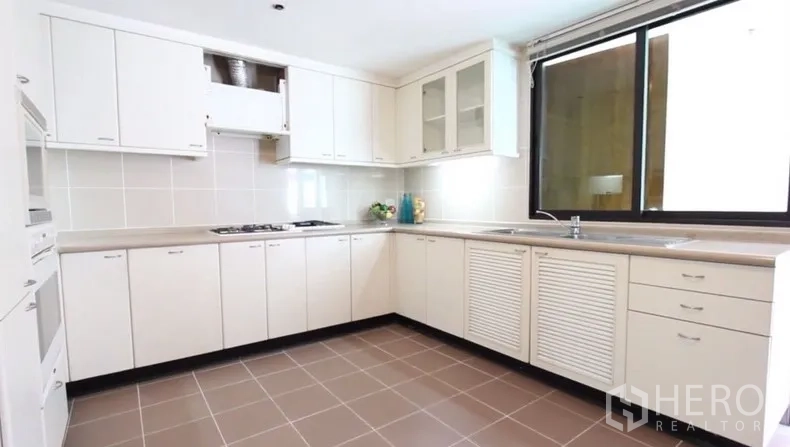 房间 出租在Khlong Toei, Bangkok - 明亮U形厨房，白色橱柜、炉灶、充足台面和大窗户。