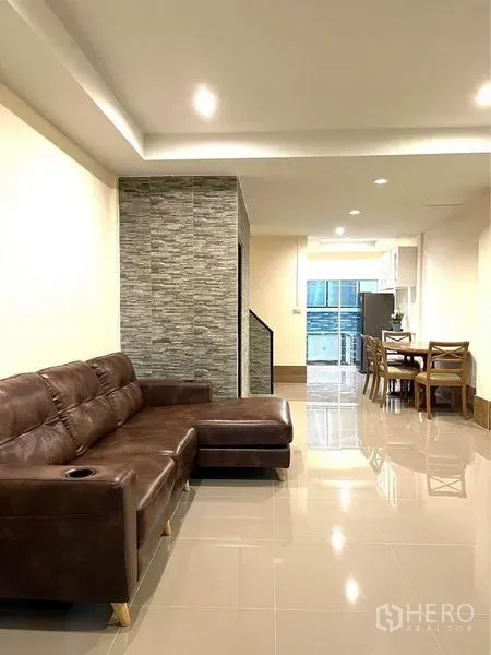 联排别墅 出租在Bang Na, Bangkok - 开放式客厅配棕色皮沙发与嵌入式照明。