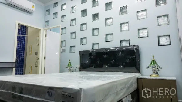 คอนโด for rent or sale in Khlong Toei, Bangkok - ห้องนอนหลักพร้อมหัวเตียงบุหนัง ผนังกระจกบล็อก และโต๊ะข้างเตียง