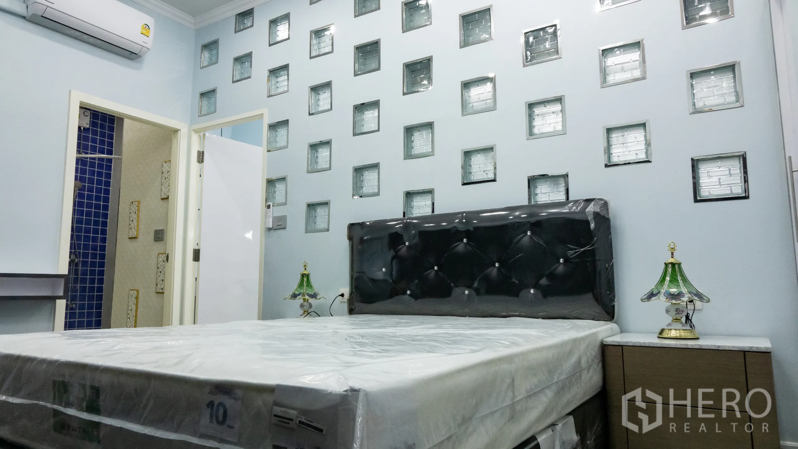 คอนโด for rent or sale in Khlong Toei, Bangkok - ห้องนอนหลักพร้อมหัวเตียงบุหนัง ผนังกระจกบล็อก และโต๊ะข้างเตียง