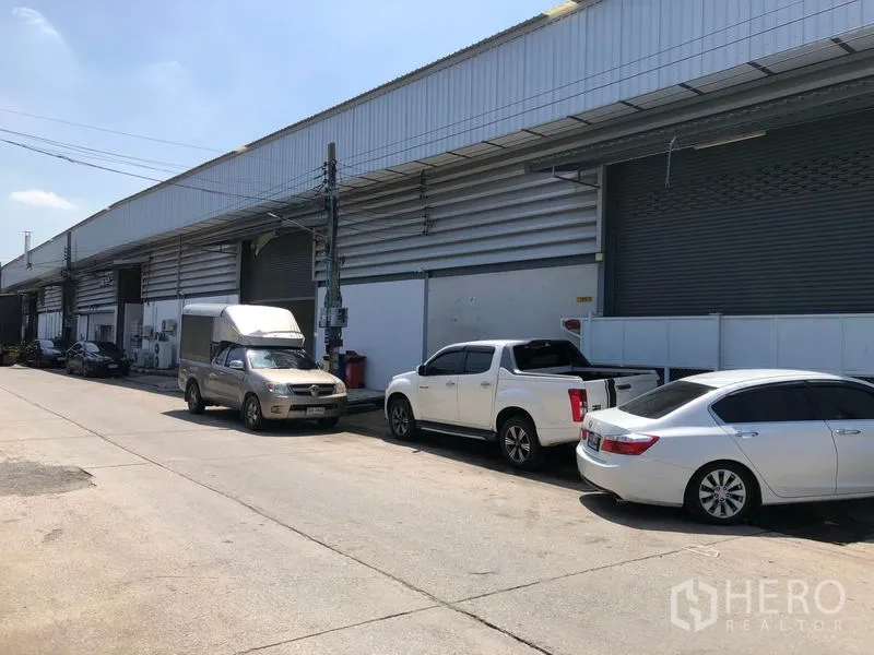 คลังสินค้า ให้เช่าในMueang Samut Prakan, Samut Prakan - อาคารโกดังเรียงรายริมถนนกว้าง มีประตูม้วนหลายบานและจอดรถริมทาง