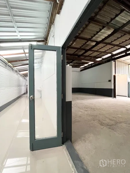 Warehouse for rent in Wang Thonglang, Bangkok - Glass door from corridor opening into the main warehouse hall with metal roof structure.