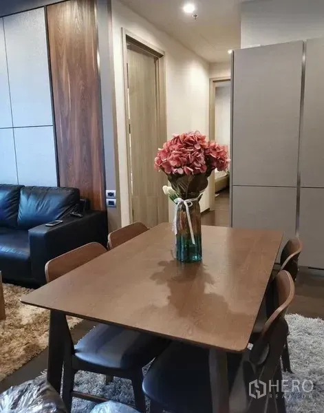 公寓 出租或出售在Watthana, Bangkok - 餐区摆放木质餐桌和四把椅子，花束点缀，邻近起居室。