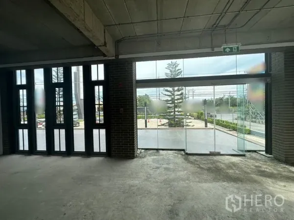 พื้นที่ขายปลีก ให้เช่าในBang Phli, Samut Prakan - มุมมองจากภายในสู่ประตูกระจกหน้าอาคาร เห็นลานด้านหน้าและผนังอิฐ