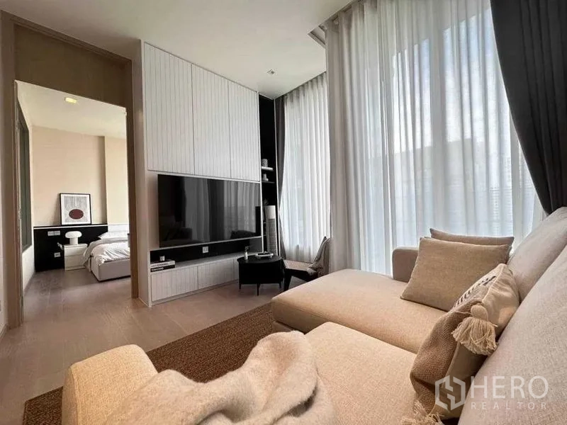 Condominium for rent in Watthana, Bangkok - Living room leading to bedroom with TV feature wall and full-height curtains