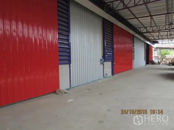货栈 出租在Bang Khen, Bangkok - 仓库外立面，多扇彩色金属卷闸门与带顶装卸区。