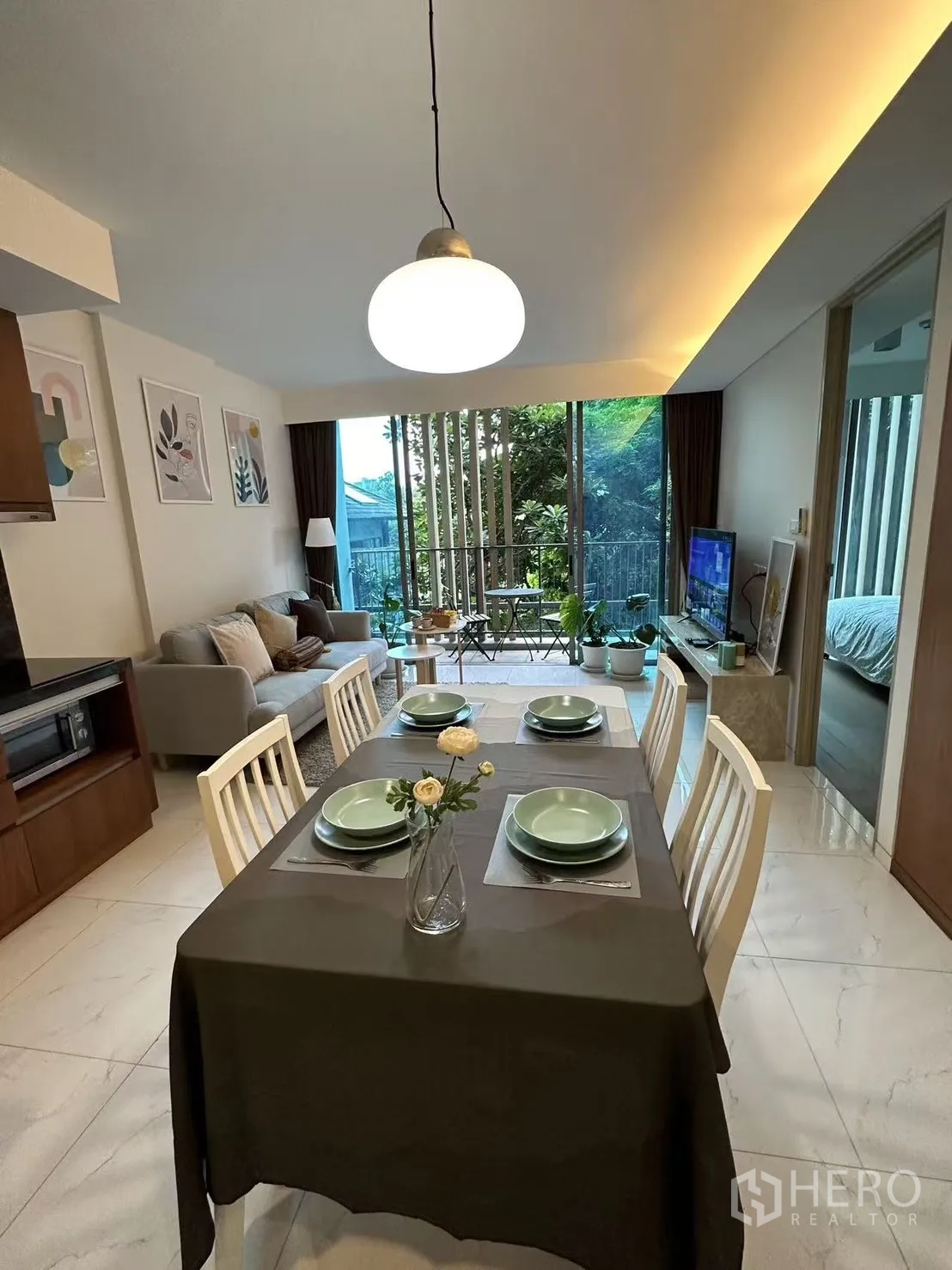 Condominium for sale in Watthana, Bangkok - Open-plan living and dining space leading to a balcony with garden outlook.