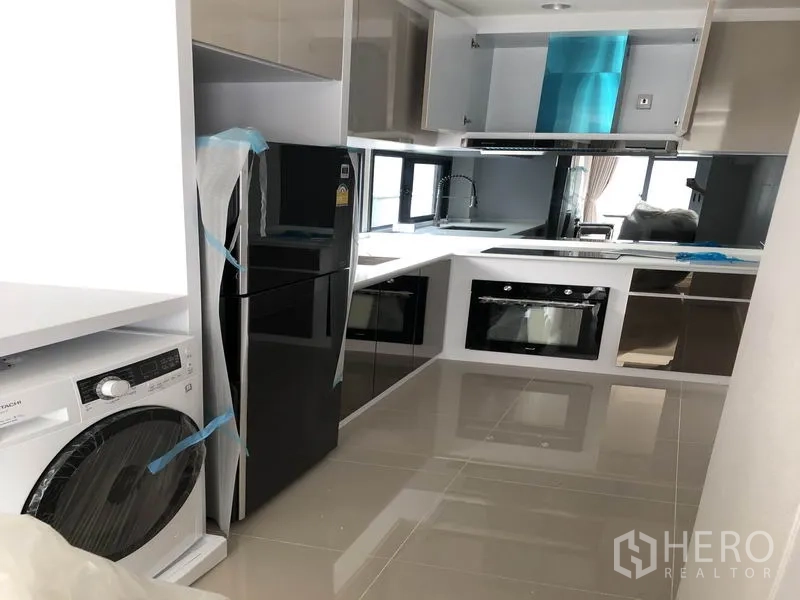 独立式住宅 出租在Prawet, Bangkok - U字型现代厨房，亮面橱柜，嵌入式烤箱，冰箱与洗衣机。