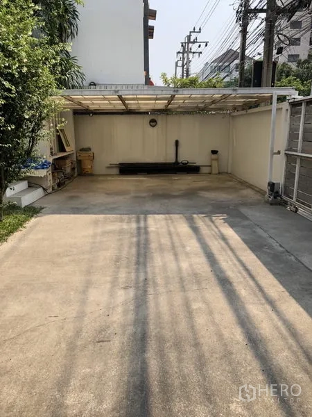 Detached House for rent in Chatuchak, Bangkok - Covered carport with concrete driveway and storage along a walled side yard.