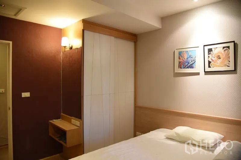 Condominium for rent in Khlong Toei, Bangkok - Second bedroom featuring a bed, framed wall art and a built-in wardrobe in warm neutral tones.